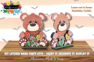 Two layered wooden bear craft kits decorated with Hallowe’en-themed items, displayed on stands. Text highlights DIY painting, decorating, and laser-cutting in Malahide, Dublin.