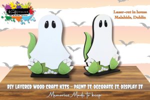 Two white and green layered wooden ghost craft kits are displayed on stands, promoting a DIY paint and decorate set. Text indicates they are laser-cut in Malahide, Dublin.