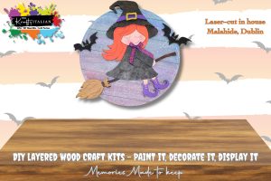 Flying witch on a broom door hanger wooden DIY craft kit made by The Krafty Italian, based in Malahide Co. Dublin. A cartoon witch with orange hair and a purple dress rides a broomstick against a round, wooden background with bats.