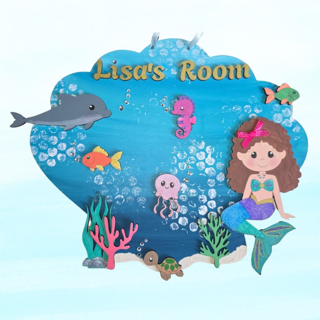 A colourful sign shaped like a seashell says Lisa's Room and features a mermaid, sea animals, corals, and bubbles on a blue background, evoking an underwater theme.