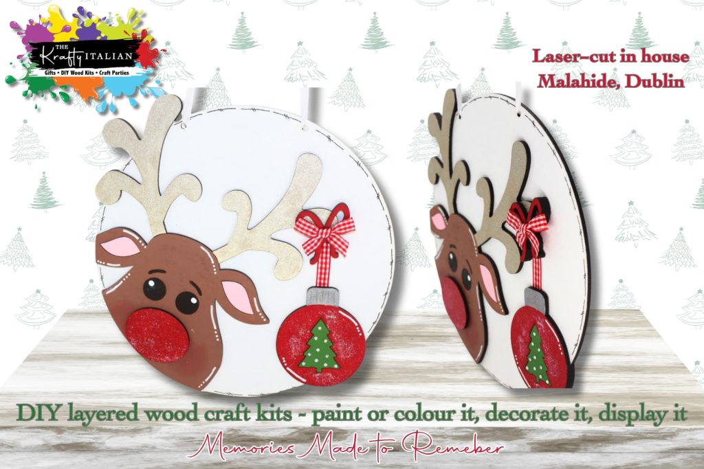 Two round, white Reindeer & Bauble Round Hanging Sign DIY kits are displayed, featuring wooden reindeer shapes with antlers, festive red bows, and Christmas baubles. The text notes they are laser-cut in Malahide, Dublin and ready for you to paint and decorate—perfect as a festive shelf sitter or to spark ideas for your next Halloween sweet basket DIY kit. The background features subtle holiday designs.